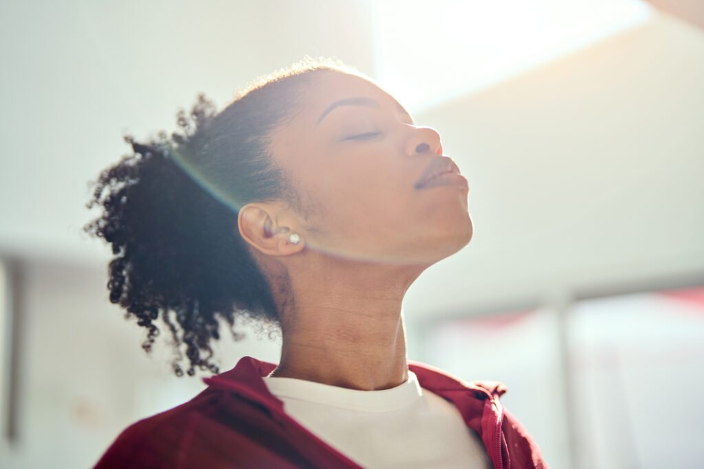 Young healthy African American woman lit with sunlight doing breathing exercise.